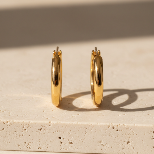 Pair of polished gold-tone hoop earrings on cream stone